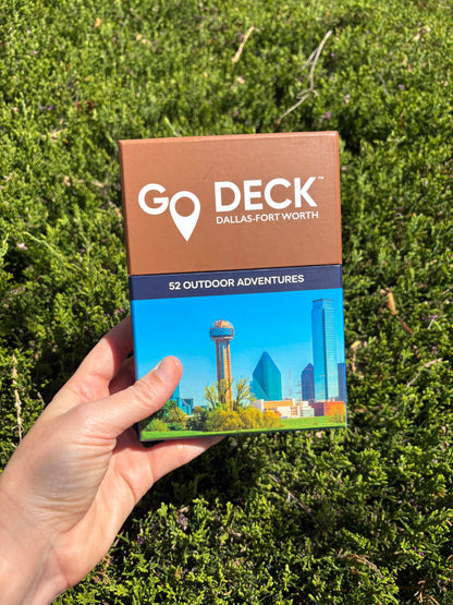 Hand holding a 'GO DECK Dallas-Fort Worth' book against a green grass background
