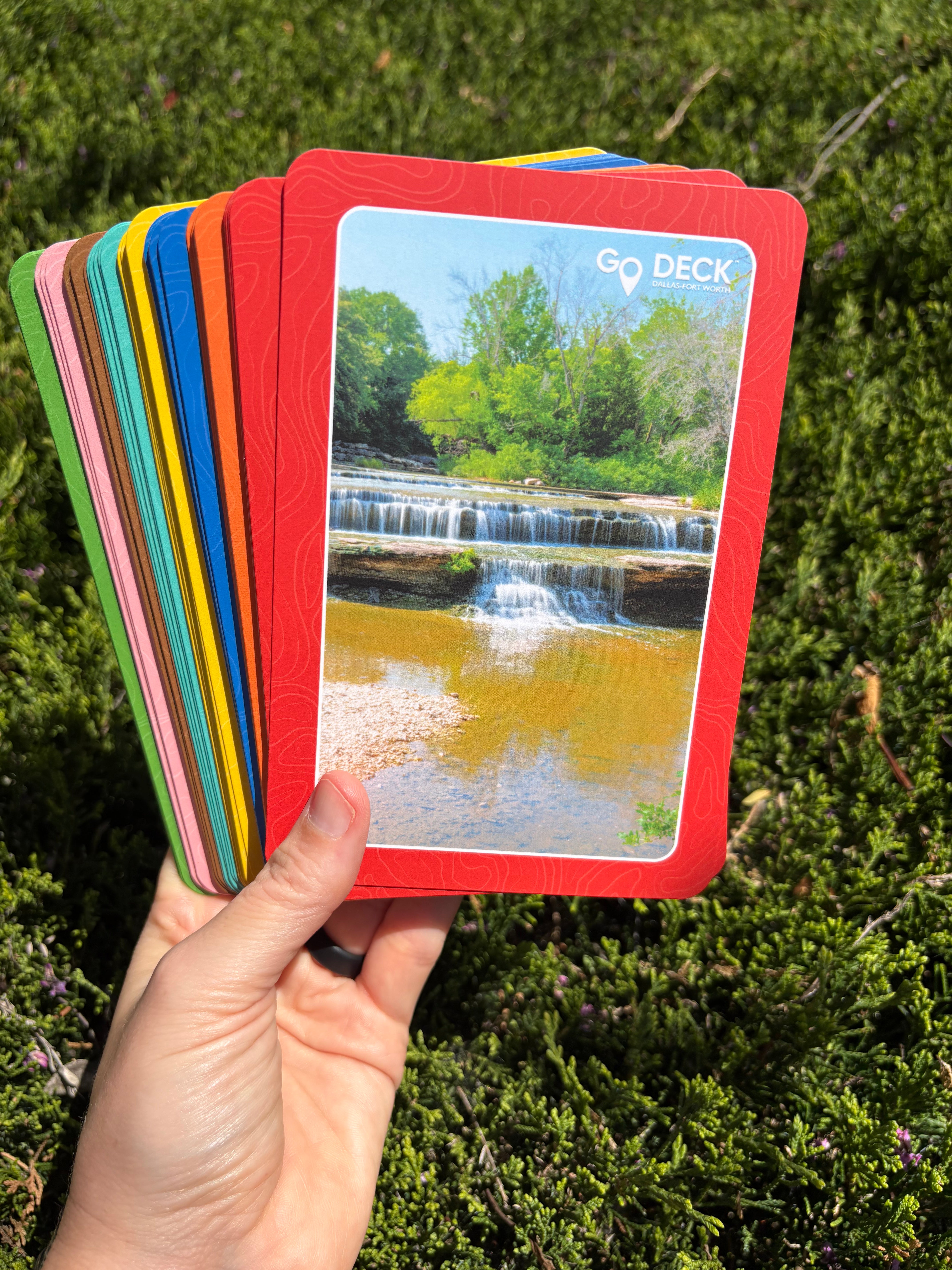 Hand holding a deck of cards with a colorful cover against a green outdoor background
