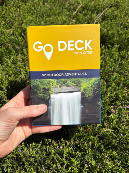 Go Deck Twin Cities outdoor adventure guide held in a hand with green grass background