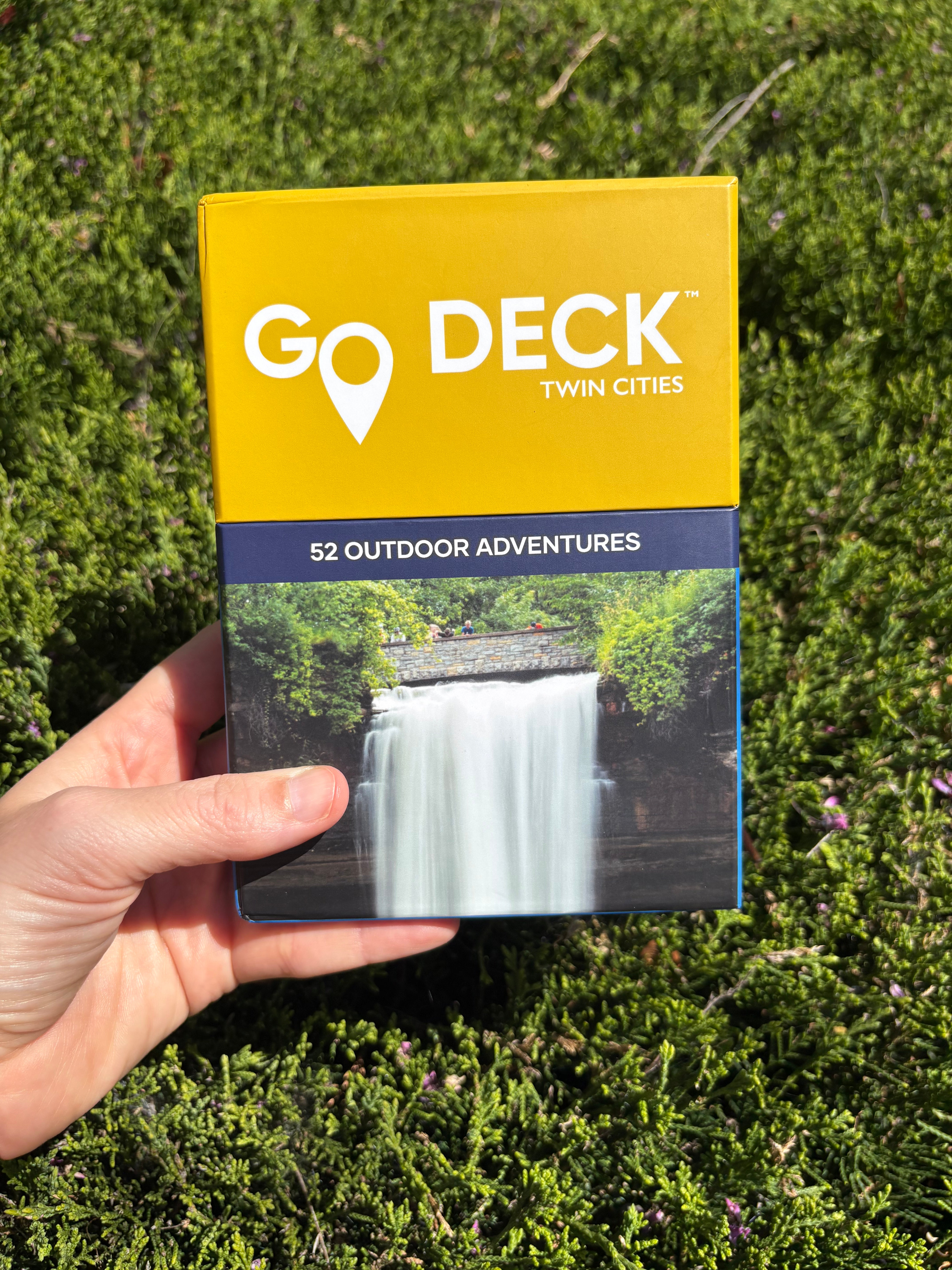 Go Deck Twin Cities outdoor adventure guide held in a hand with green grass background