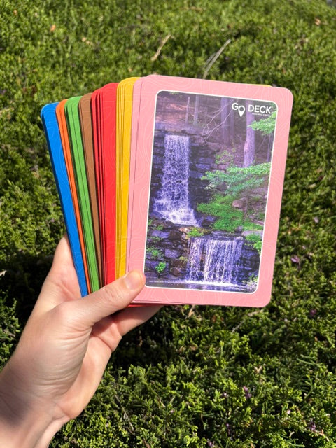 Hand holding a stack of colorful cards with a scenic image on a grassy background